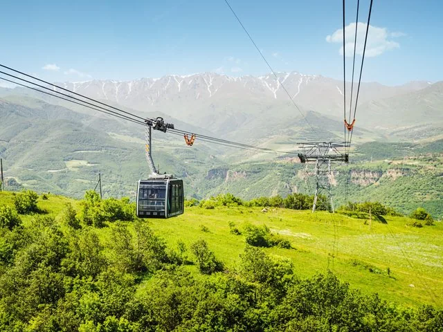Téléphérique passant au-dessus de collines verdoyantes vers des montagnes enneigées en Arménie