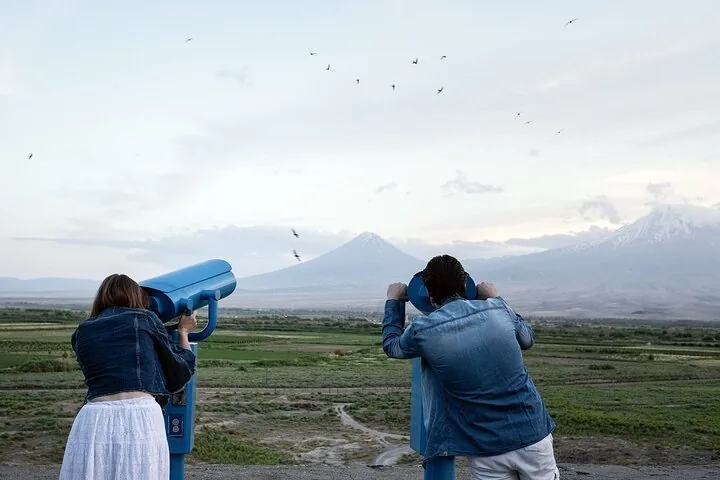 Two people looking through binoculars at Mount Ararat across the plains